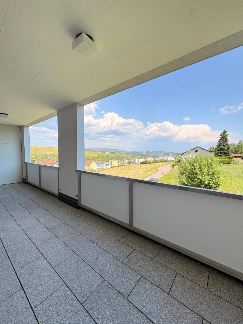 Geräumiger Balkon mit Fliesenboden und Panoramablick auf die grüne Landschaft und den Horizont.
