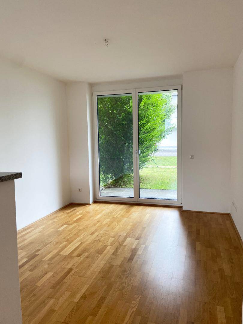 Heller Raum mit Holzboden und großer Glasschiebetür, die Zugang zum grünen Außenbereich bietet.