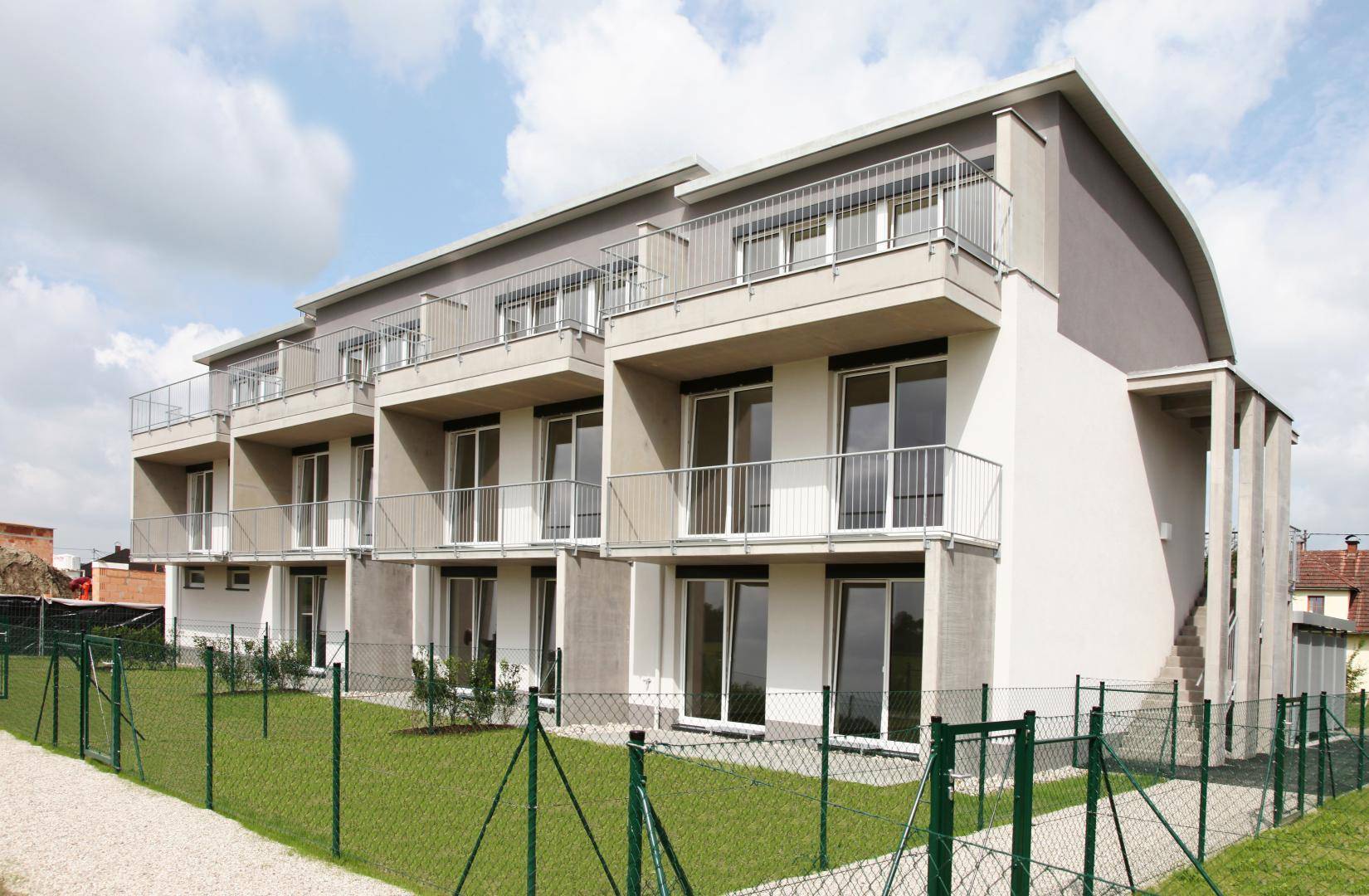 Modernes Mehrfamilienhaus mit mehreren Balkonen und gepflegter Grünfläche im Vordergrund.