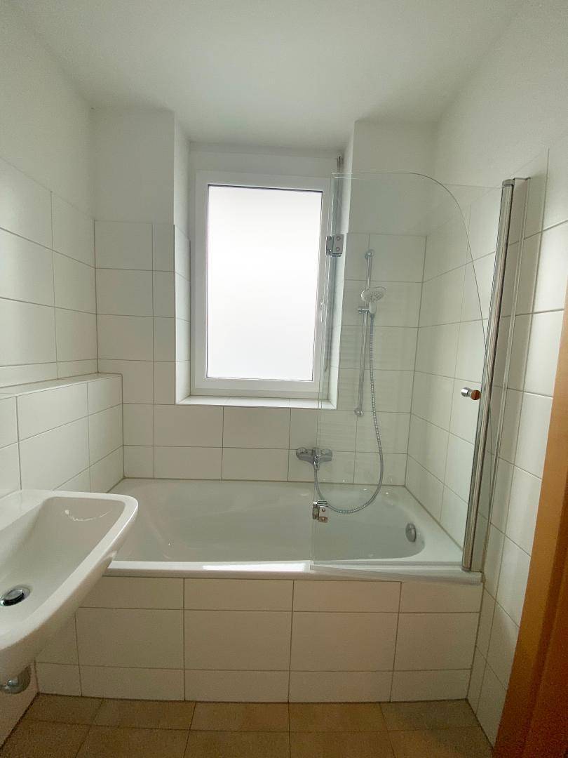 Helles Badezimmer mit Badewanne, Duschfunktion, Einzelwaschbecken und einem Fenster für Tageslicht.