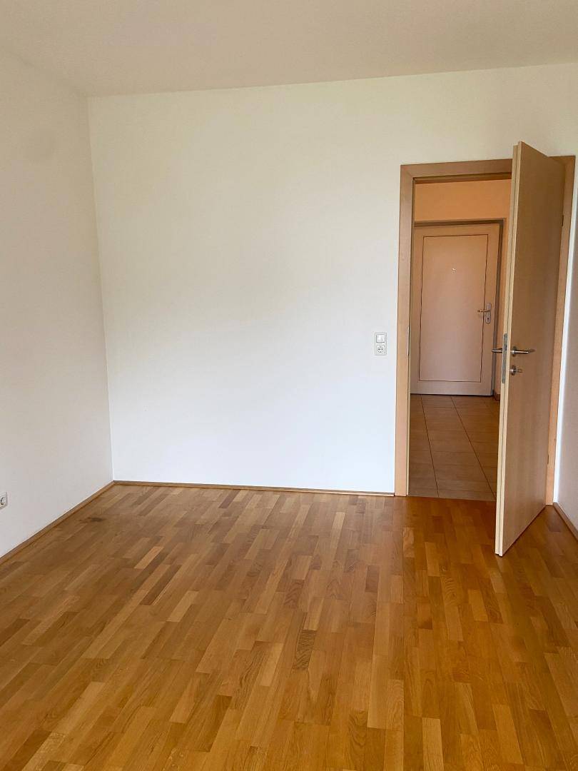 Leerer Raum mit hellem Holzboden und weiß gestrichenen Wänden, mit Zugang zu einem Flur.