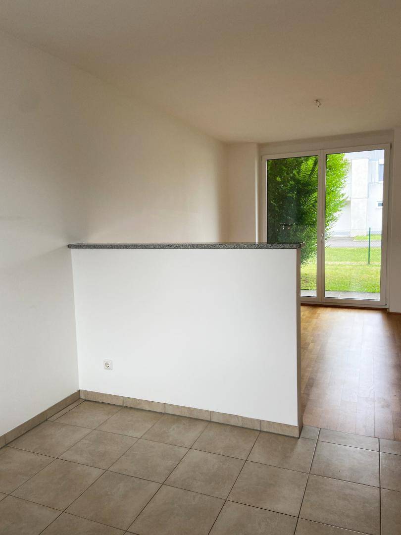 Übergangsbereich zwischen Wohnraum und Küche, gekennzeichnet durch eine halbhohe Trennwand und große Fenster.