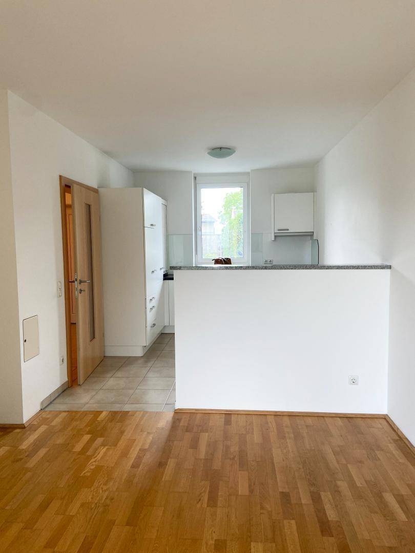 Offener Wohnbereich mit Holzboden, der in eine helle Küche mit Fliesenboden übergeht.