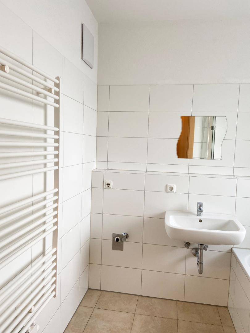 Modern gefliestes Badezimmer mit Einzelwaschbecken, beheiztem Handtuchhalter und weißer Wandgestaltung.