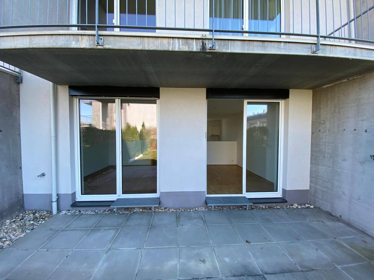 Erdgeschoss-Terrasse mit Fliesenboden und Zugang zu den Innenräumen, überdacht von einem Balkon.