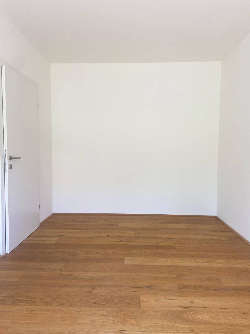 Leeres Zimmer mit Holzboden und weiß gestrichenen Wänden, bereit zur Einrichtung.