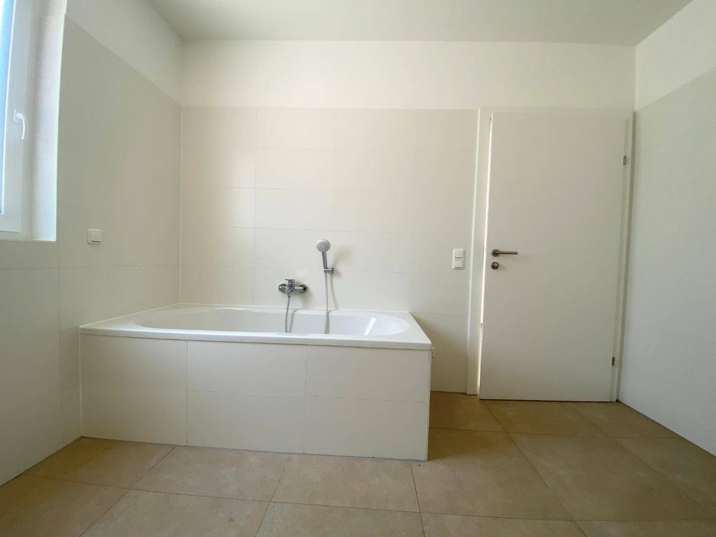 Helles Badezimmer mit Badewanne, Fenster und neutralen Fliesen.