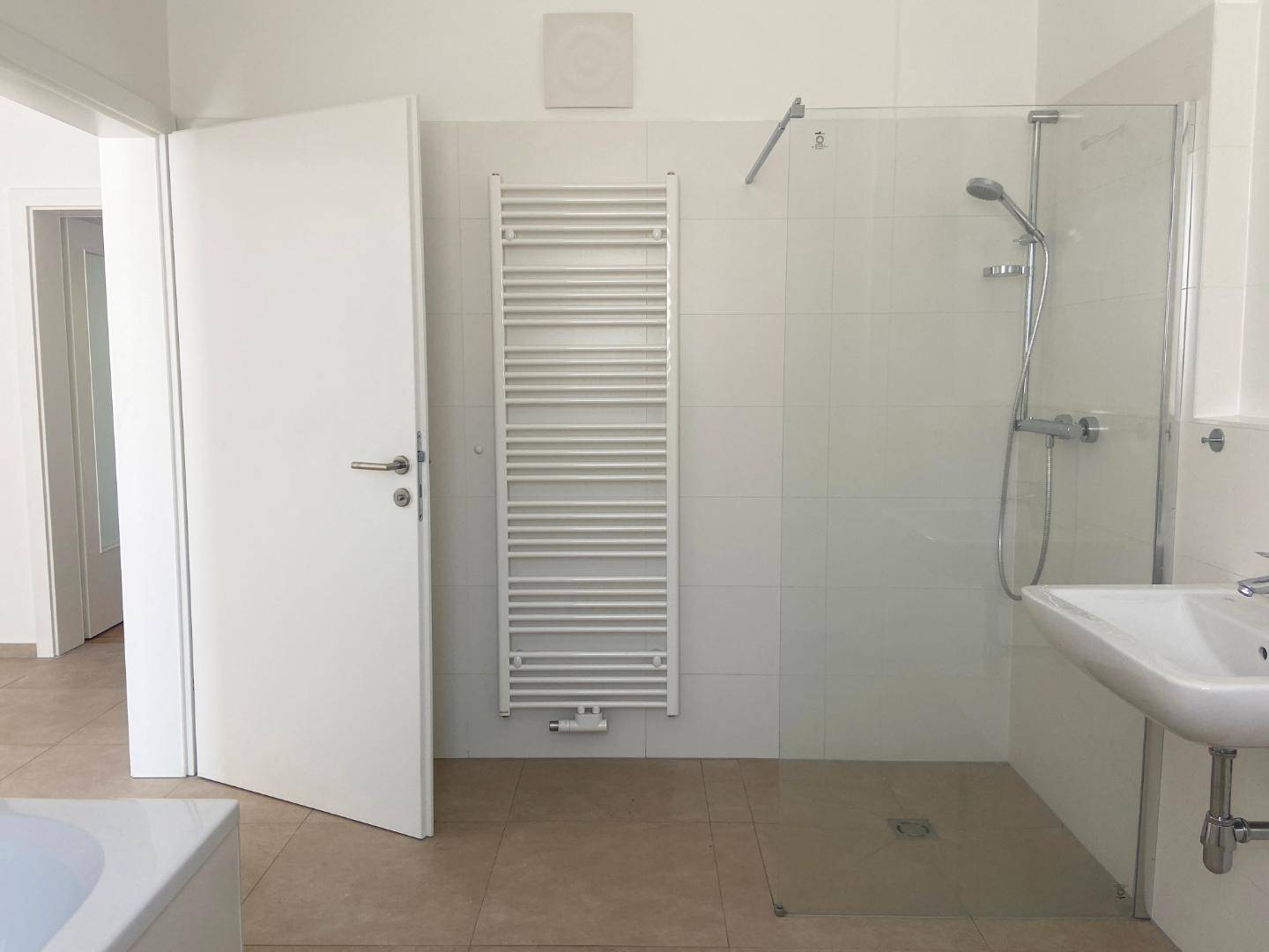 Badezimmer mit ebenerdiger Dusche, Handtuchheizkörper und Fliesenboden.