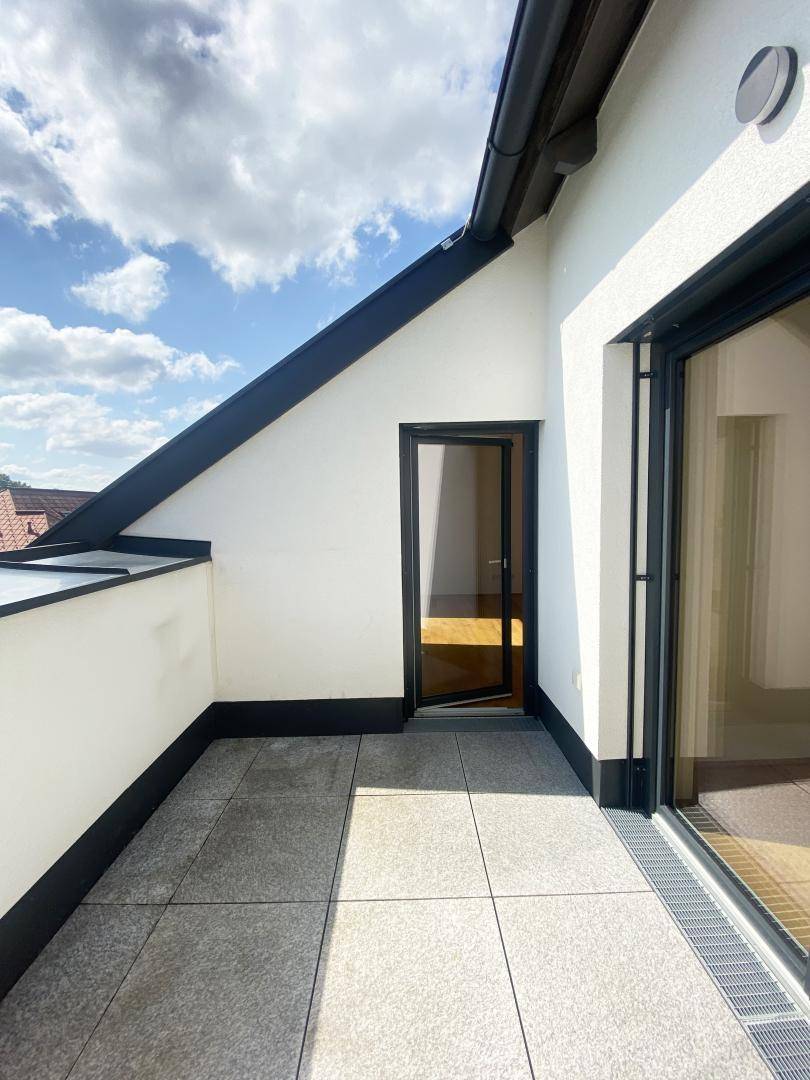 Sonniger Außenbereich mit Fliesenboden und Zugang zum Innenraum, geschützt durch eine Dachschräge.