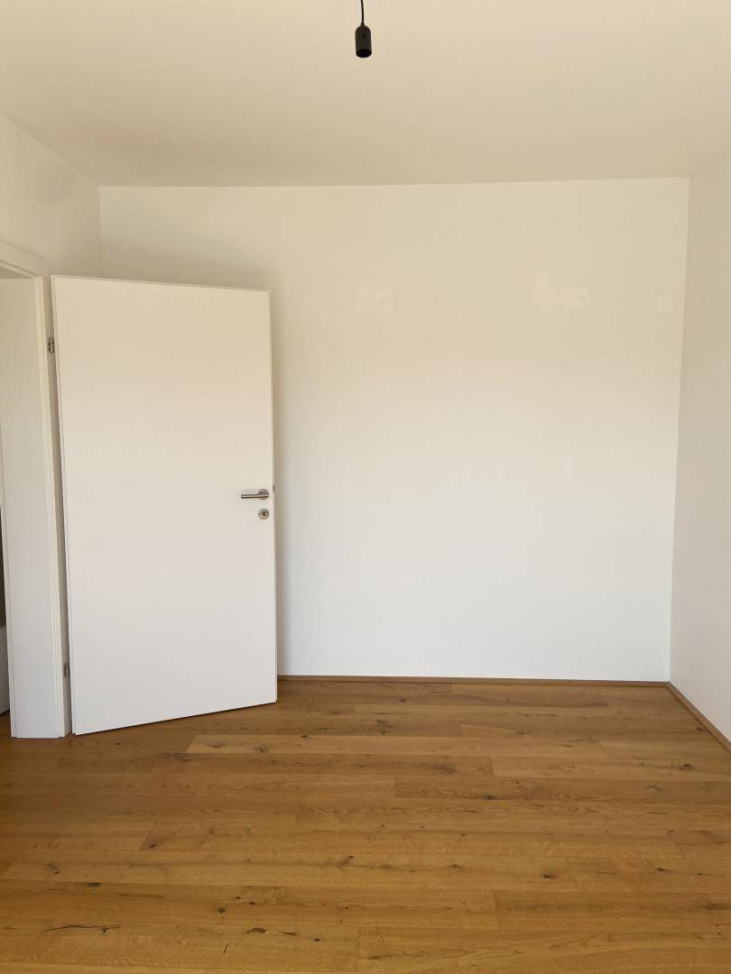 Leeres Zimmer mit Holzboden und weißen Wänden, bereit zur individuellen Gestaltung.