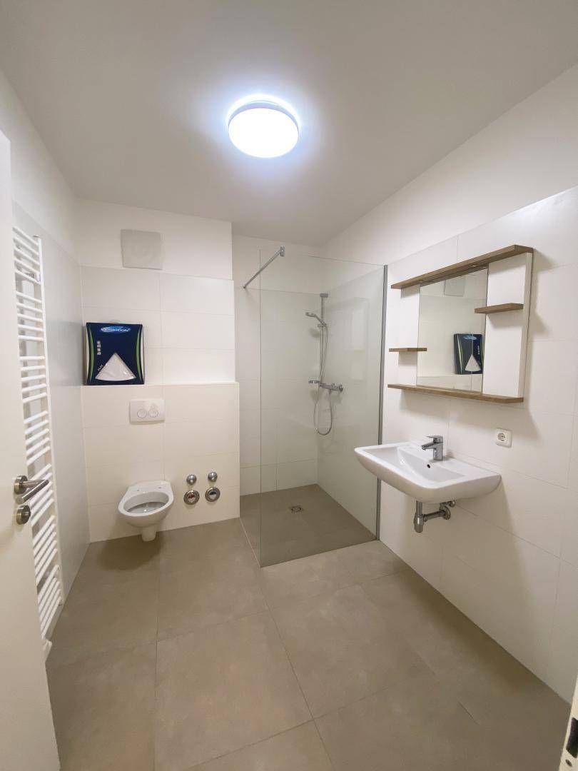 Modernes Badezimmer mit begehbarer Dusche, Wand-WC, Einzelwaschbecken und Handtuchheizkörper.