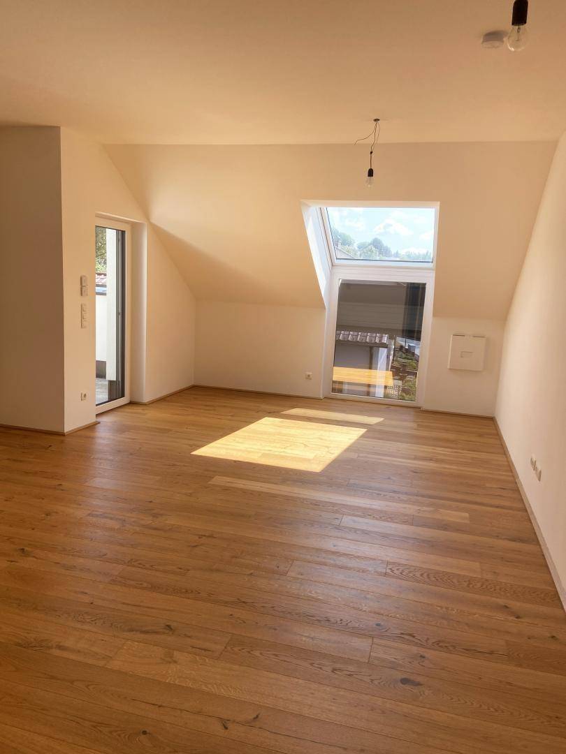 Heller Wohnraum mit Holzboden, Dachschräge und großem Dachfenster, das viel Sonnenlicht hereinlässt.