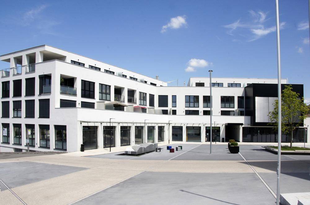 Modernes Geschäftsgebäude mit weißer Fassade, großen Fenstern und einem gepflegten Vorplatz.