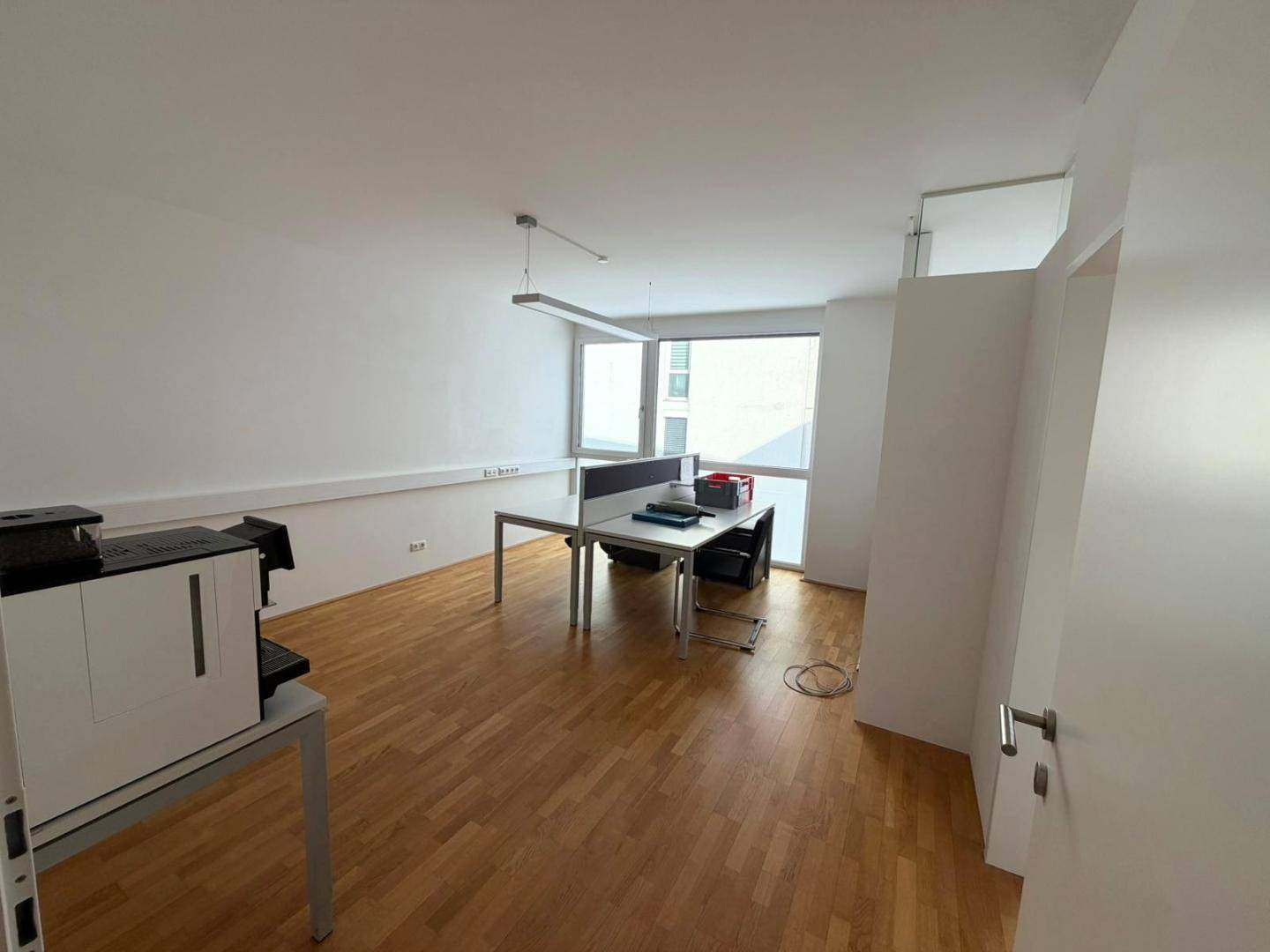 Heller Büroraum mit Holzboden, großen Fenstern und einem Arbeitsplatz, ideal für konzentriertes Arbeiten.