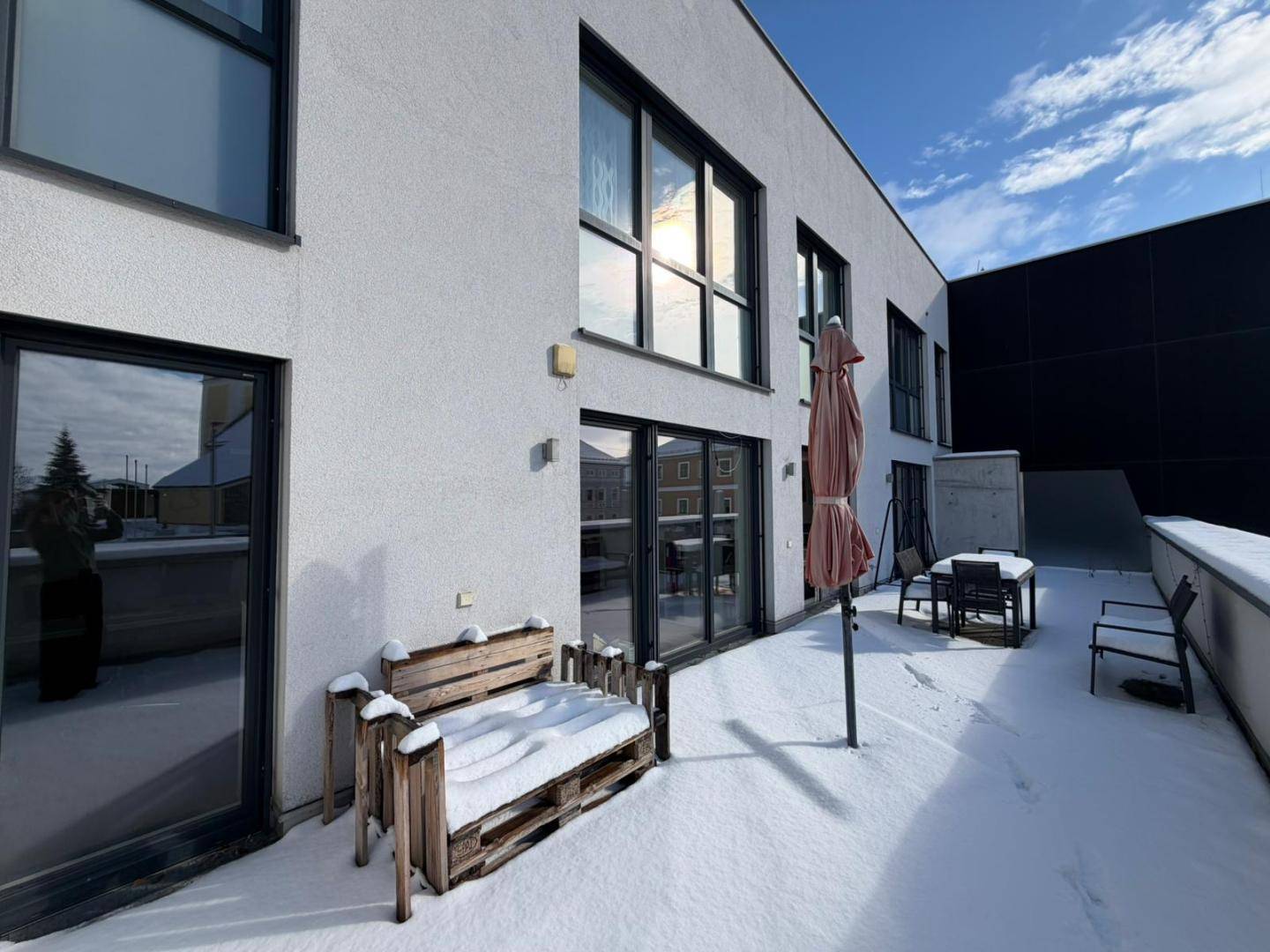 Große Außenterrasse im Winter mit Schnee, Sitzgelegenheiten und Blick auf die moderne Gebäudefassade.