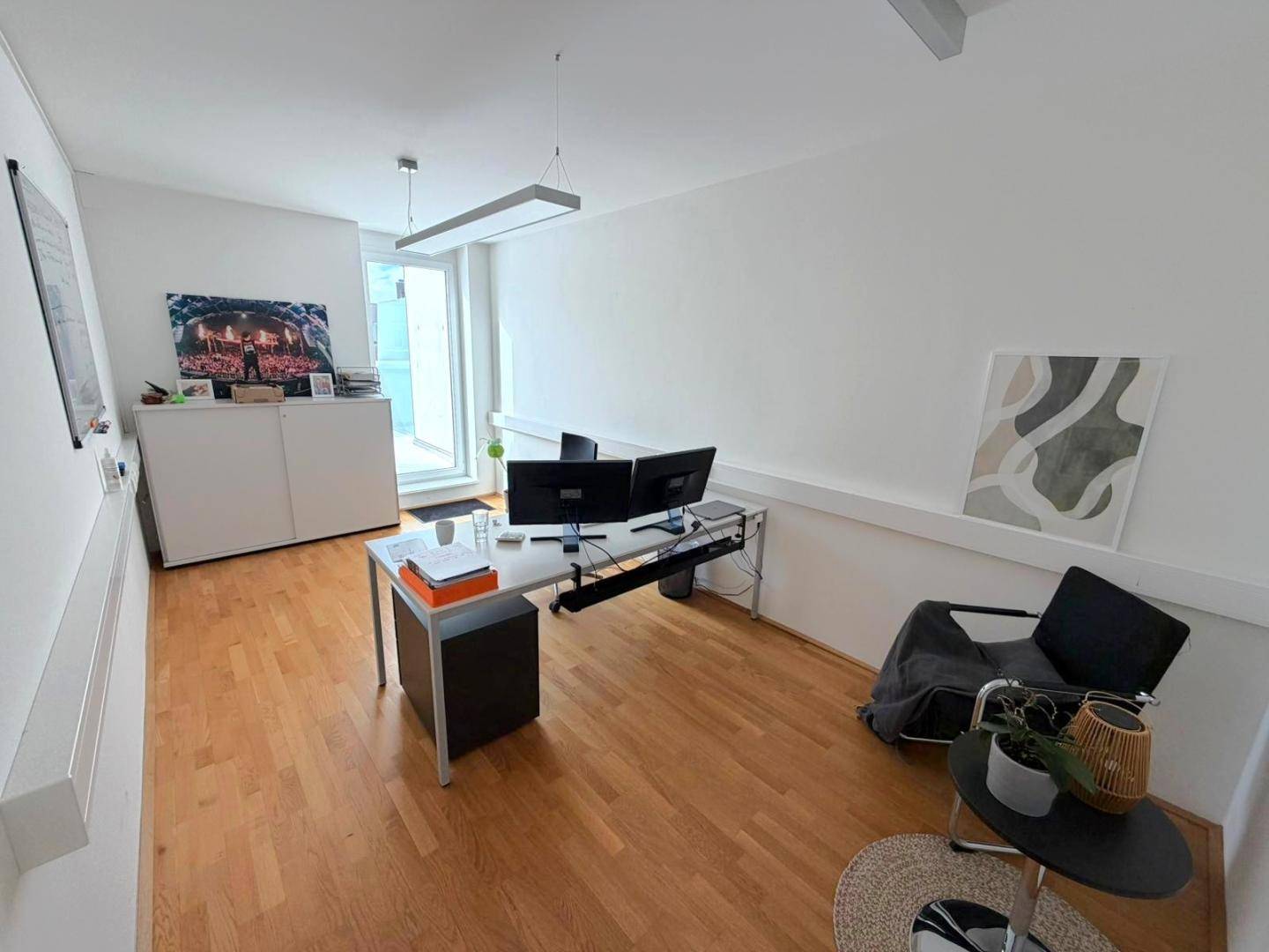 Gemütliches Büro mit Holzboden, Schreibtisch, bequemen Stühlen und einem Fenster mit Zugang nach draußen.
