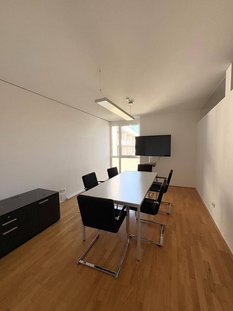 Besprechungsraum mit Holzboden, großem Tisch, Stühlen und einem Wandfernseher für Präsentationen.