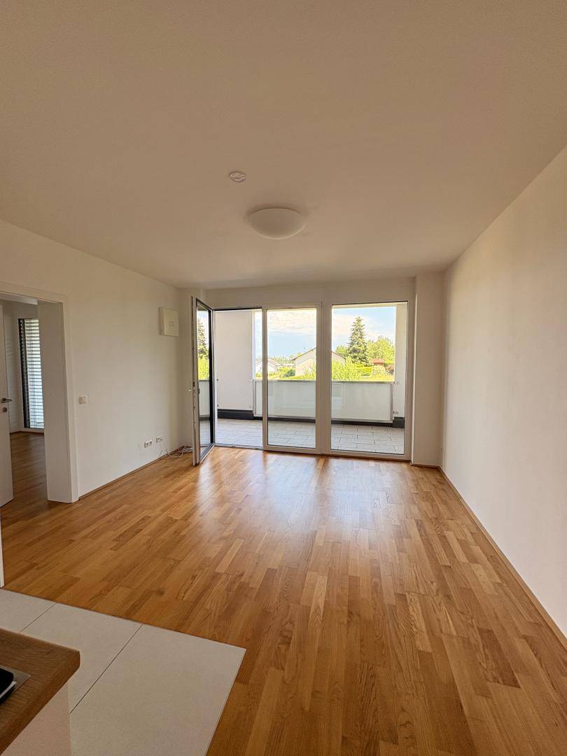 Helles Wohnzimmer mit Parkettboden und großzügigem Zugang zu einem Balkon mit Weitblick.
