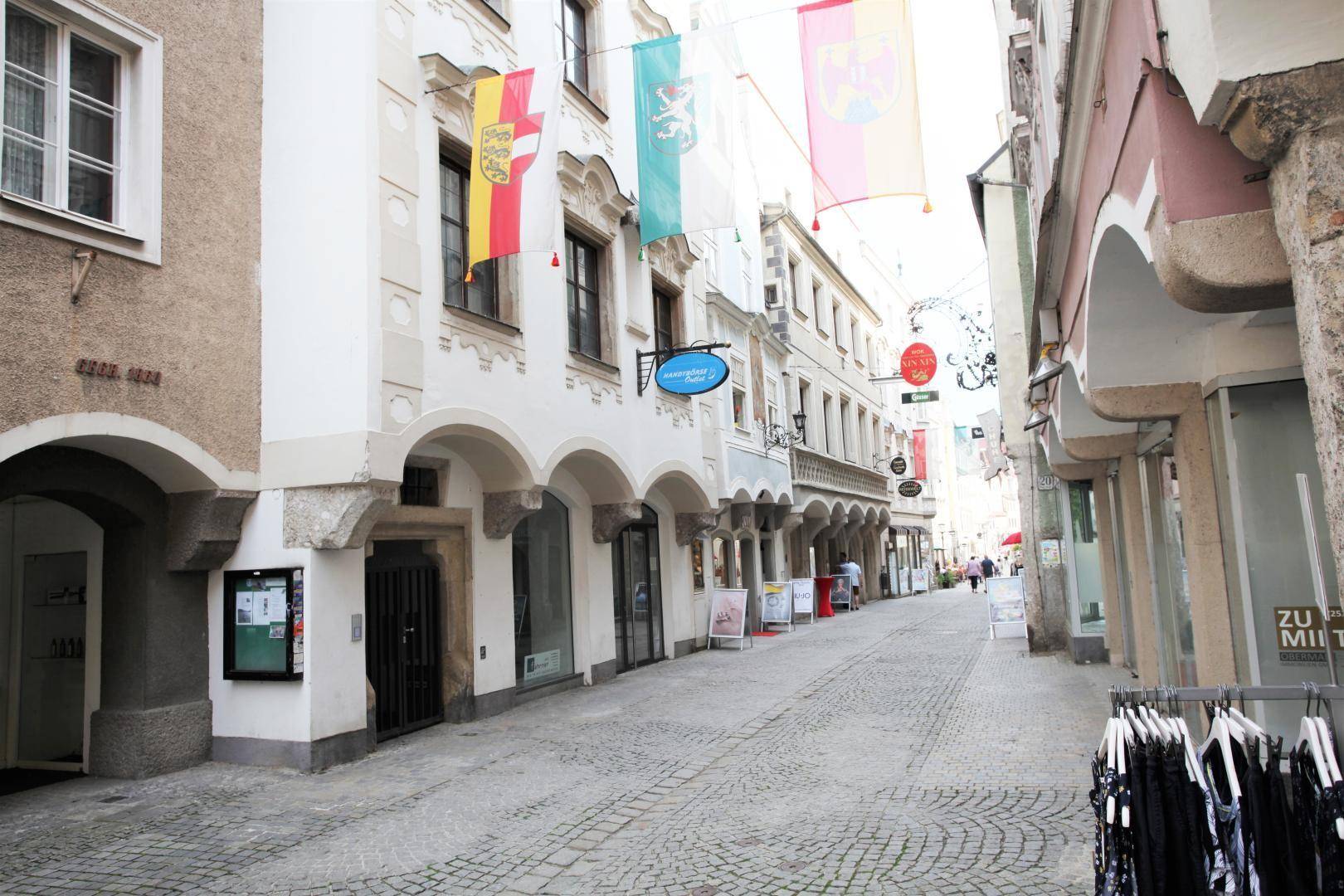 Historische Gasse mit Kopfsteinpflaster, alten Gebäuden und Geschäften, geschmückt mit Fahnen.
