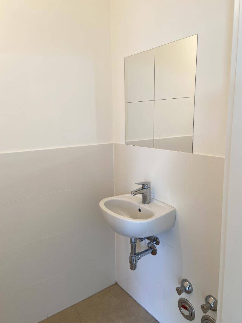 Kleines Gäste-WC mit Waschbecken und Spiegel, in schlichtem, funktionalem Design gehalten.