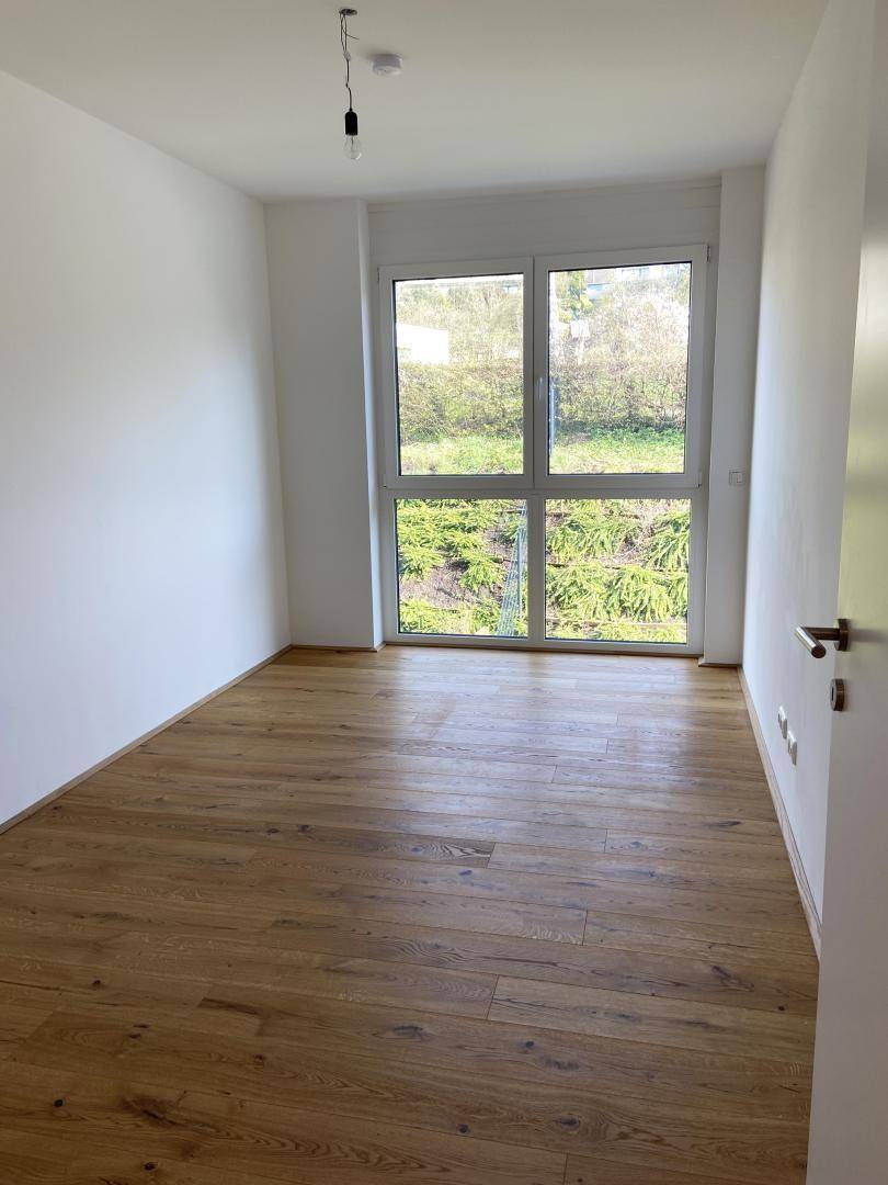 Geräumiges Schlafzimmer mit Holzboden und großem Fenster, das viel Tageslicht hereinlässt.