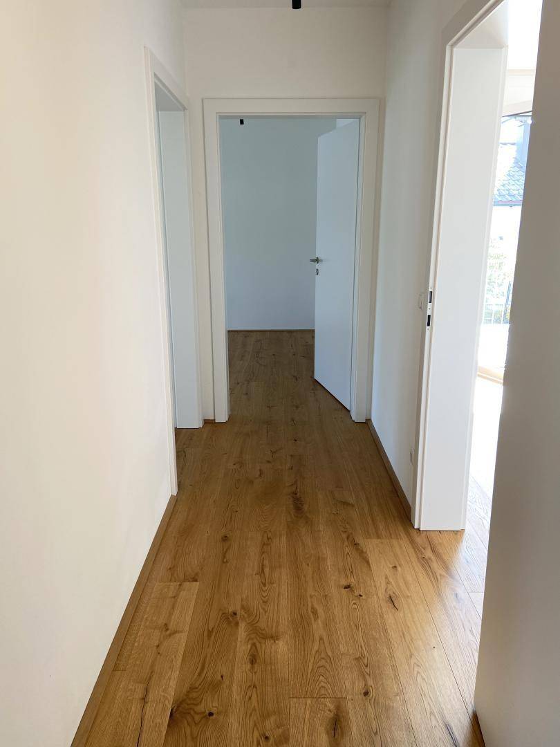 Langer, heller Flur mit Holzboden, der zu verschiedenen Zimmern der Wohnung führt.