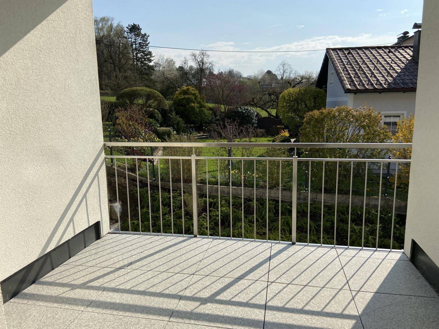 Sonniger Balkon mit Fliesenboden und Metallgeländer, bietet einen schönen Blick ins Grüne.