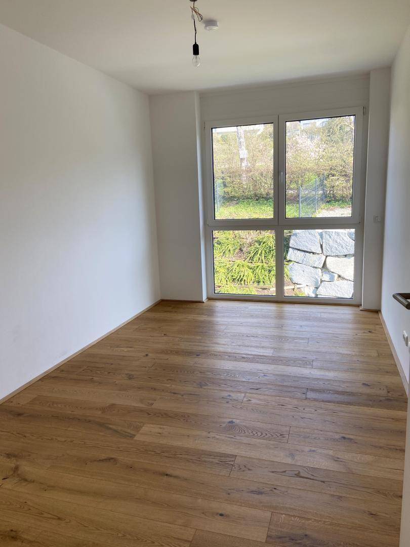 Helles Schlafzimmer mit Holzboden und großem Fenster, das einen Blick auf einen Steingarten bietet.