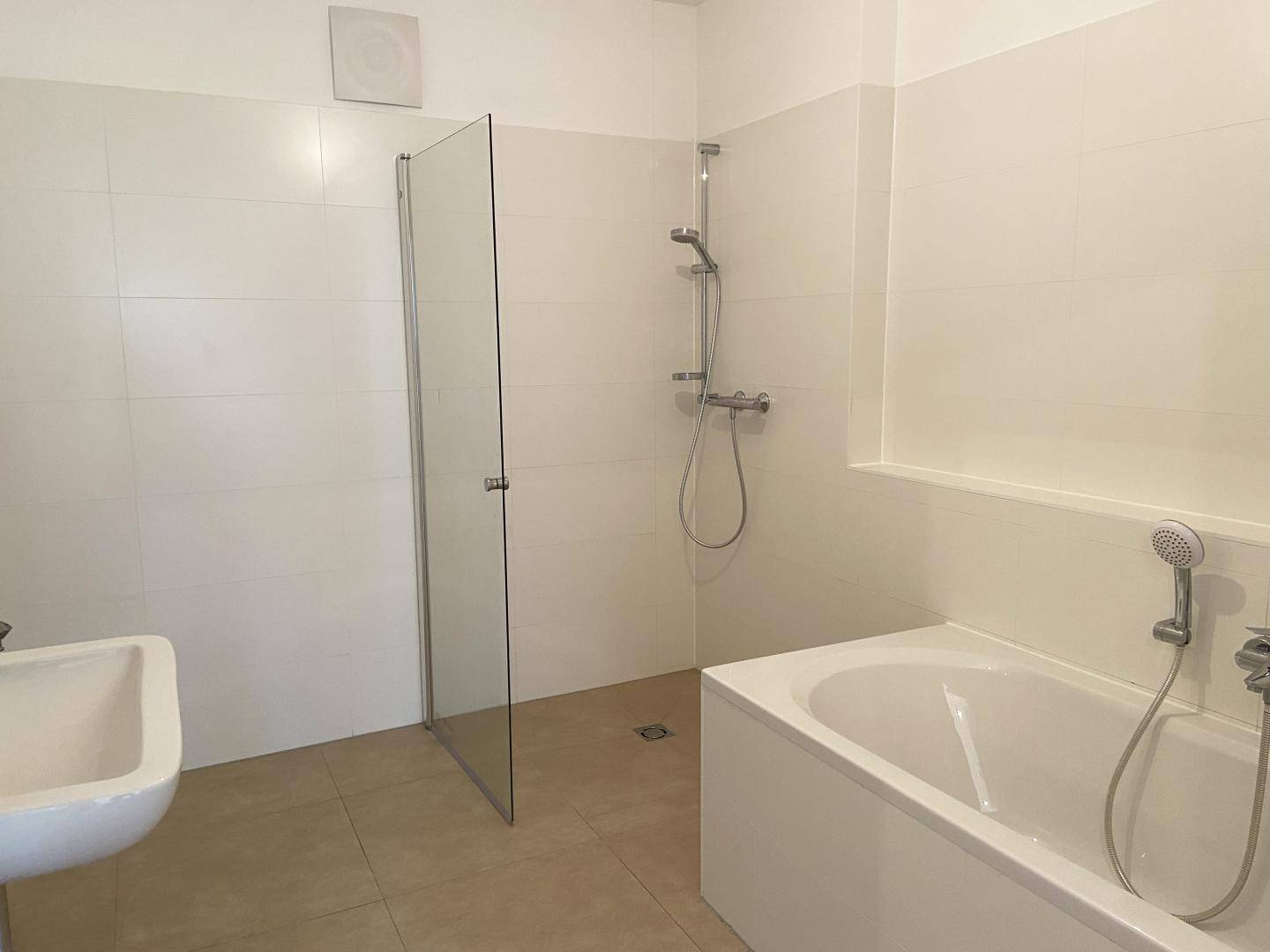 Modernes Badezimmer mit Badewanne, Duschbereich mit Glaswand und hellem Fliesenboden.