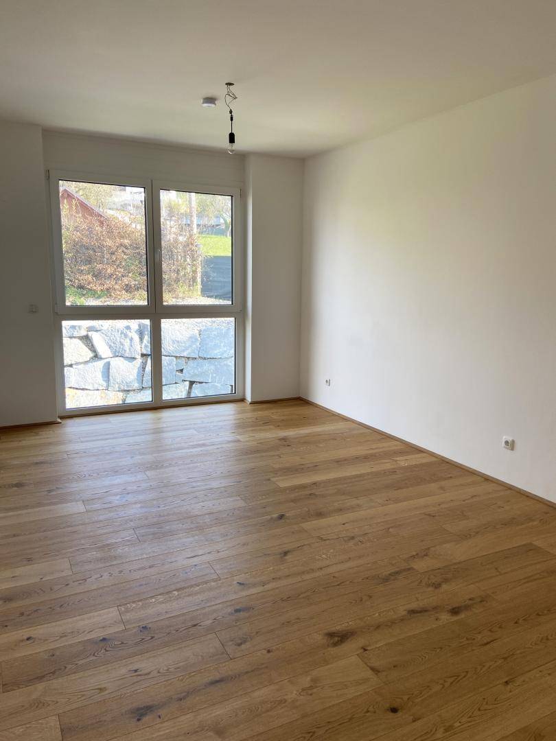 Helles Schlafzimmer mit Holzboden und großem Fenster, das einen Blick auf einen Steingarten bietet.