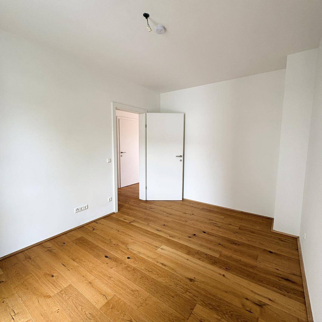 Leeres Zimmer mit Parkettboden und zwei Türen, die zu anderen Räumen führen.