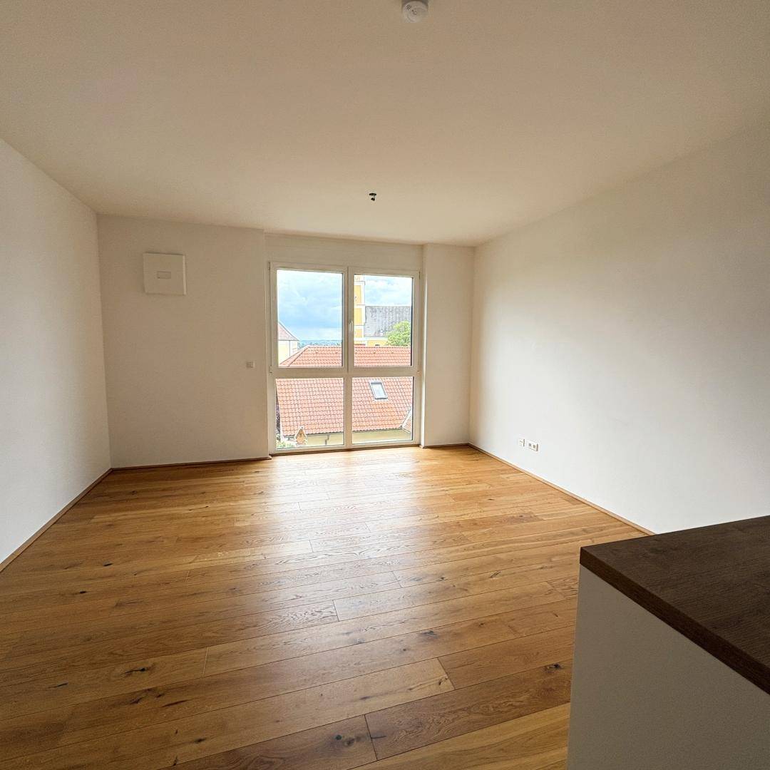Heller Raum mit Parkettboden und Zugang zu einem Balkon oder einer kleinen Terrasse.