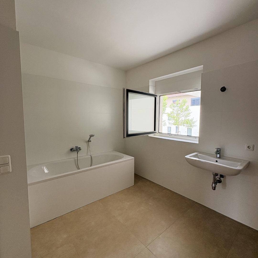 Helles Badezimmer mit Badewanne, Waschbecken, Fliesenboden und einem Fenster für Tageslicht.
