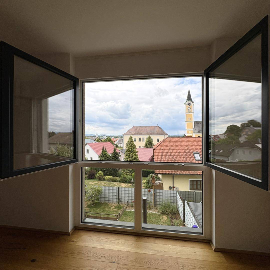 Weitblick aus dem Fenster über Dächer, Gärten und einen Kirchturm in der Ferne.