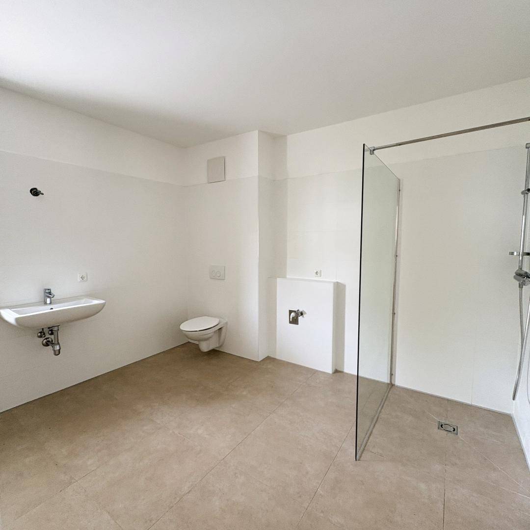 Modernes Badezimmer mit Fliesenboden, wandhängendem WC und einer geräumigen begehbaren Dusche.