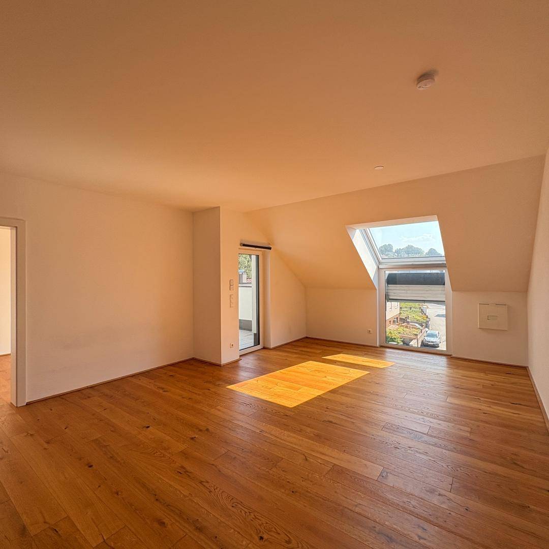 Helles Wohnzimmer mit Holzboden, Dachschräge und großem Dachfenster, Blick nach draußen.
