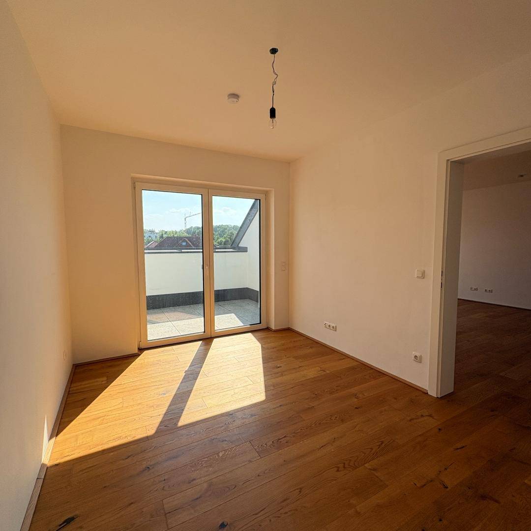 Schlafzimmer mit Holzboden und Zugang zu einer sonnigen Terrasse, viel natürliches Licht.