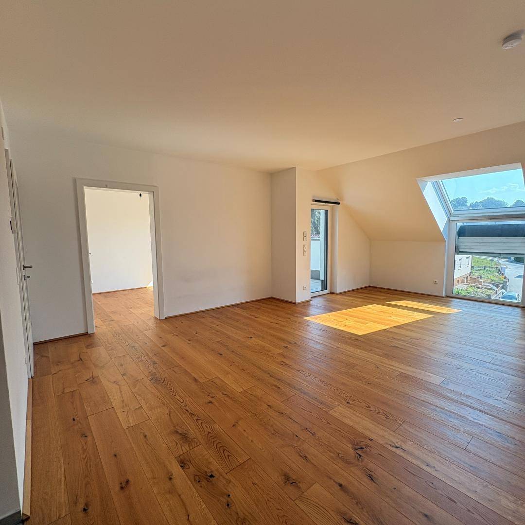 Geräumiges Wohnzimmer mit Holzboden, Dachschräge und großem Dachfenster, viel Tageslicht.