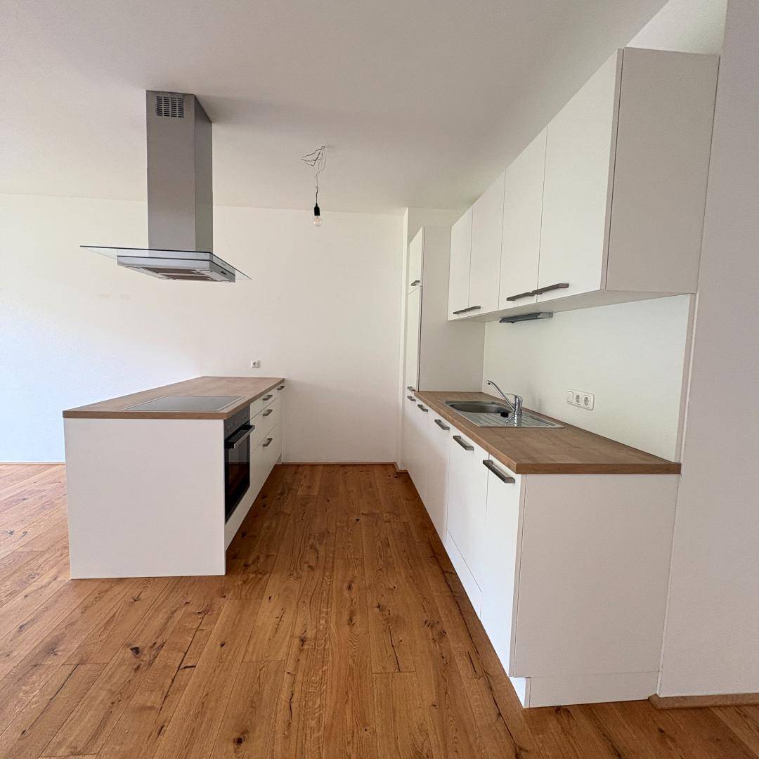 Moderne Einbauküche mit weißen Schränken, Holztheke und integrierten Geräten in neuwertigem Zustand.