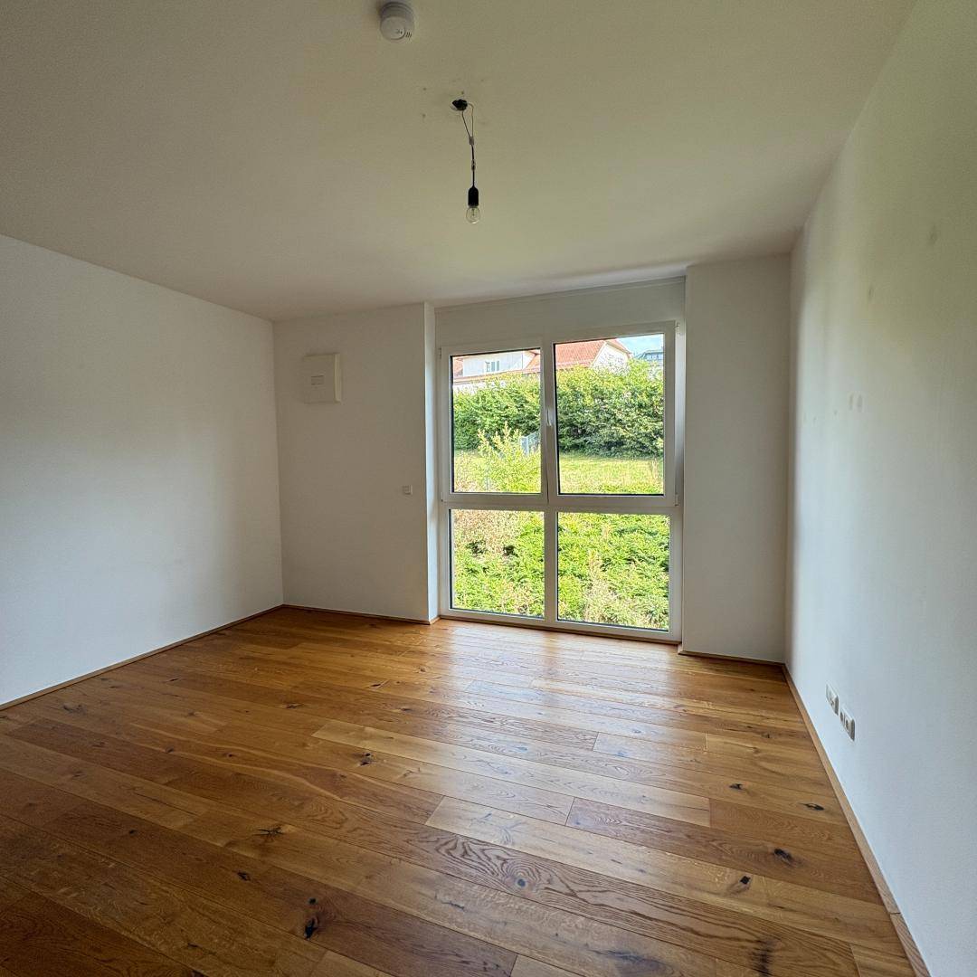 Helles Zimmer mit großen Fenstern, Blick ins Grüne und elegantem Holzfußboden.