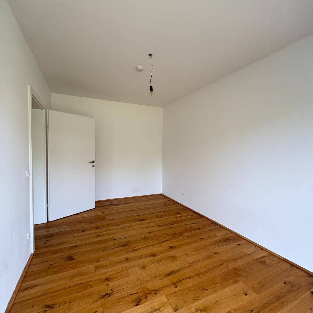 Unmöbliertes Zimmer mit neuem Holzfußboden und weiß gestrichenen Wänden.