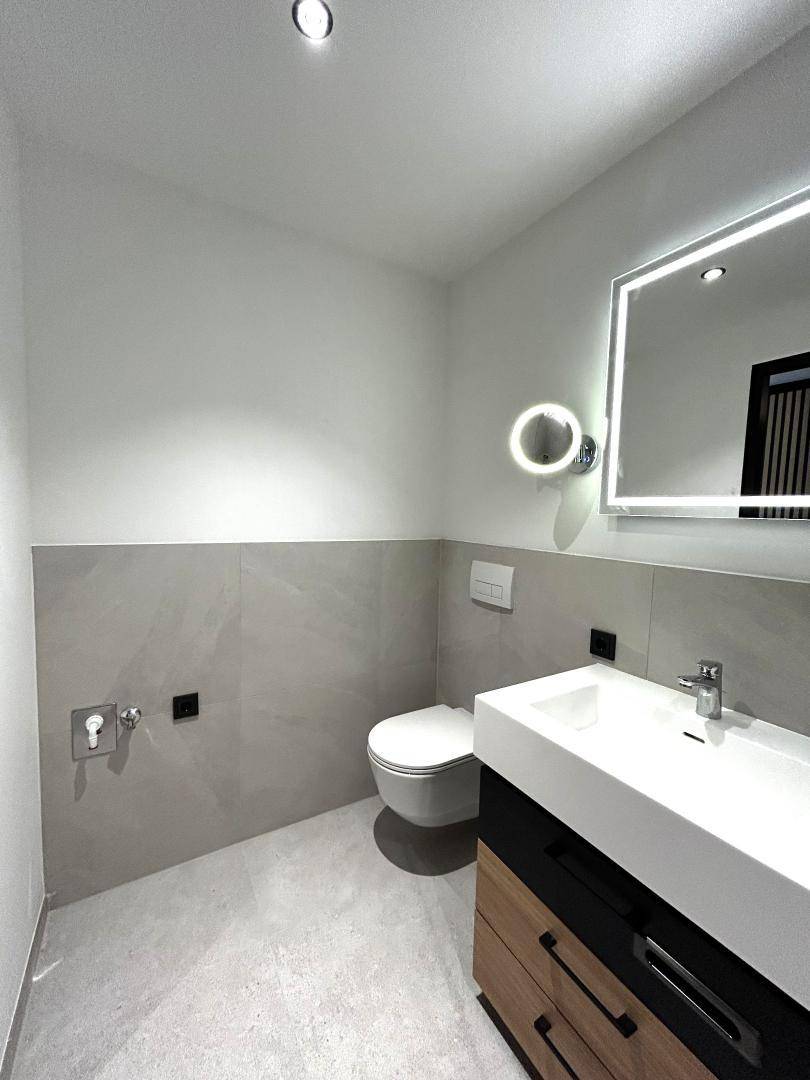 Helles Badezimmer mit wandhängendem WC, Einzelwaschbecken und beleuchtetem Spiegelschrank.