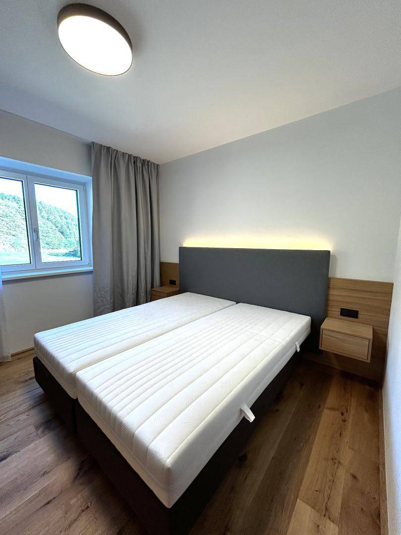 Modernes Schlafzimmer mit Doppelbett, Holzboden und integrierter Beleuchtung am Kopfteil.