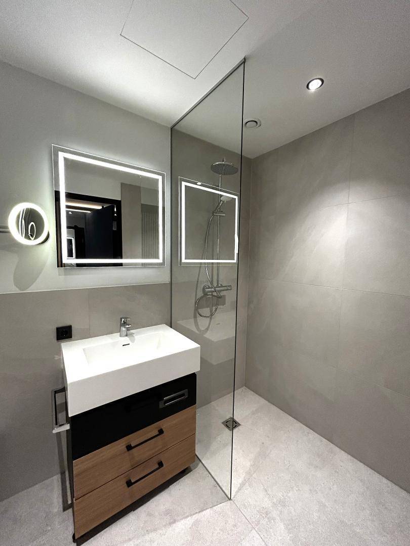 Modernes Badezimmer mit begehbarer Dusche, Einzelwaschbecken und beleuchtetem Spiegel.