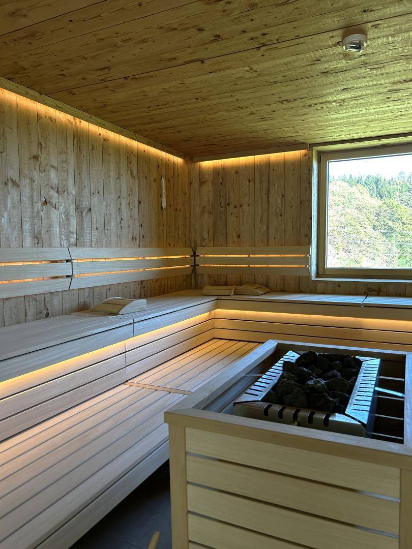 Moderne Holzsauna mit breiten Bänken, indirekter Beleuchtung und Fenster.