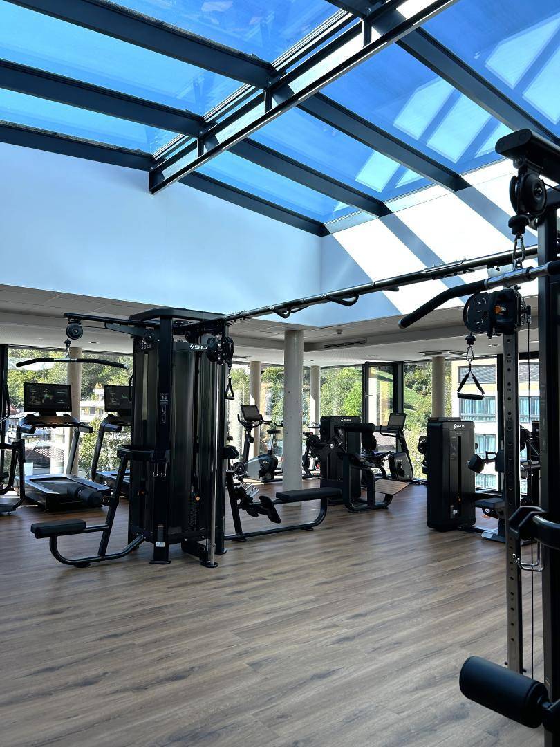 Geräumiger Fitnessraum mit vielfältigen Geräten, großen Fenstern und Glasdach für viel Licht.