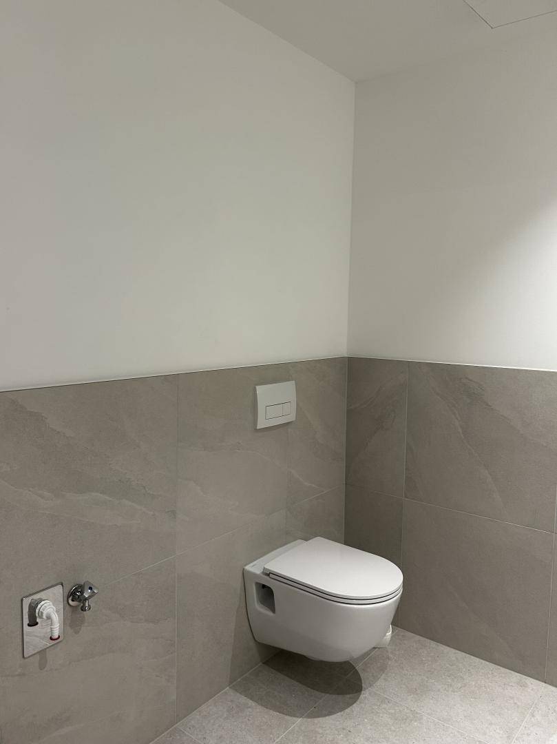 Helles WC mit wandhängender Toilette und modernen grauen Fliesen an Wänden und Boden.
