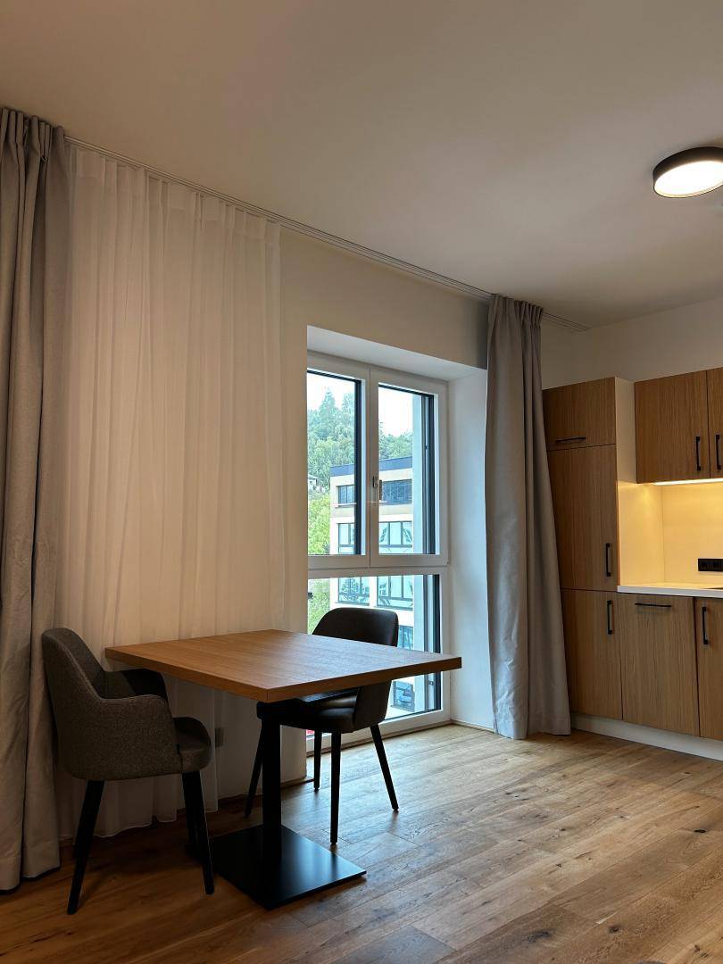 Heller Essbereich mit Holztisch und Stühlen, angrenzend an eine moderne Küchenzeile mit Fenster.
