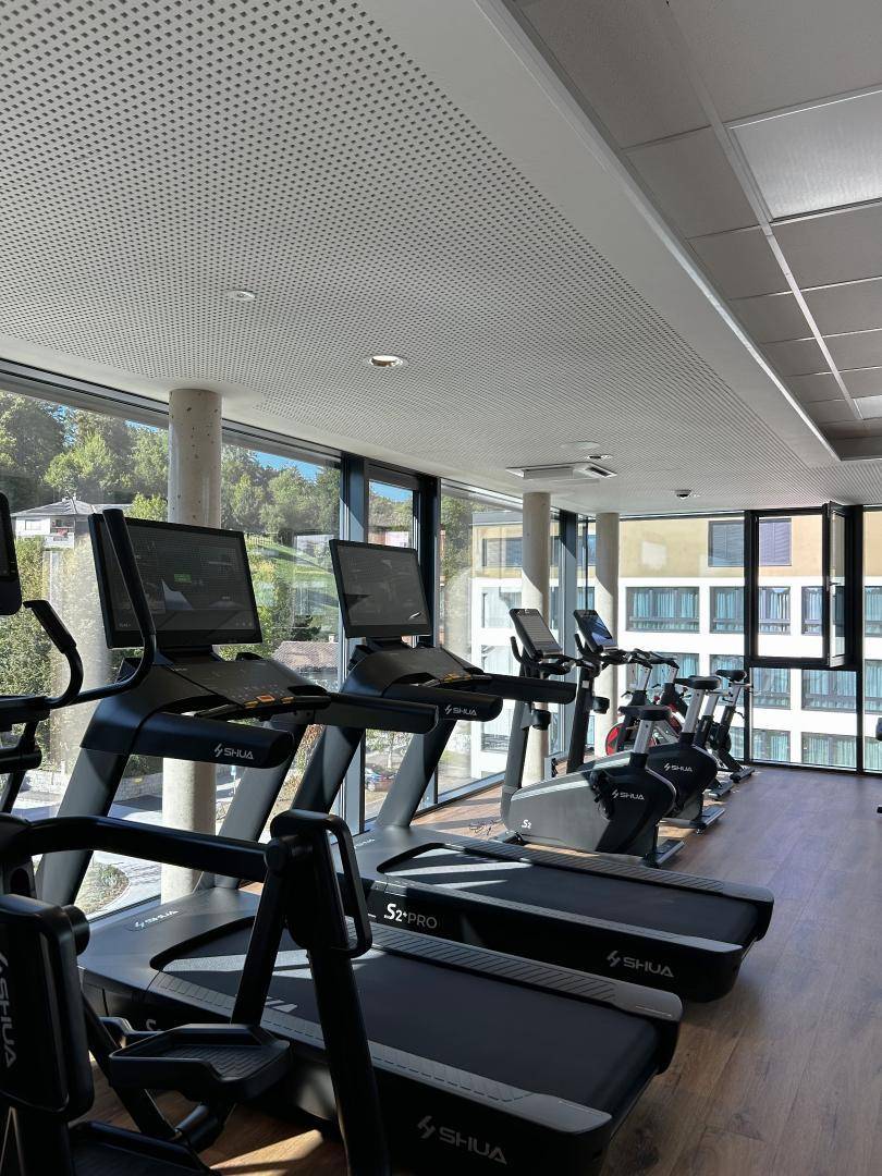 Modernes Fitnessstudio mit Laufbändern und großen Fenstern, die viel Tageslicht hereinlassen.