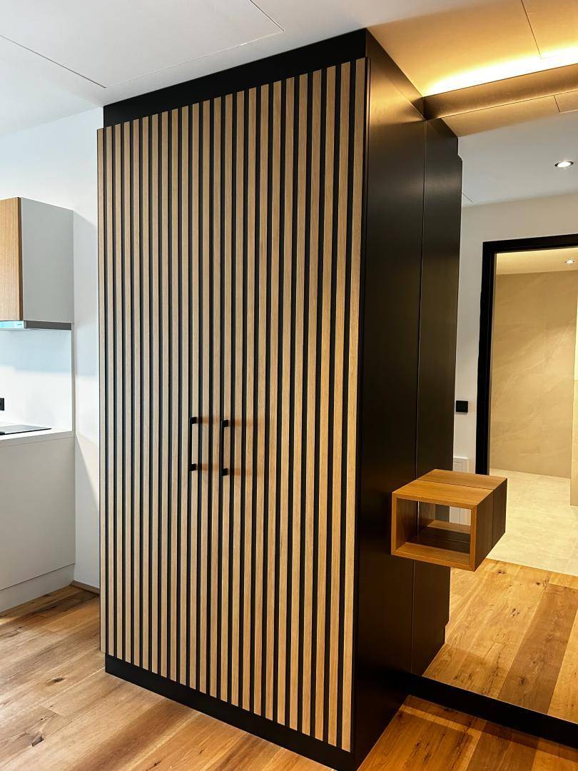 Stilvoller Flur mit vertikalen Holzlamellen und integriertem Stauraum, modern gestaltet.